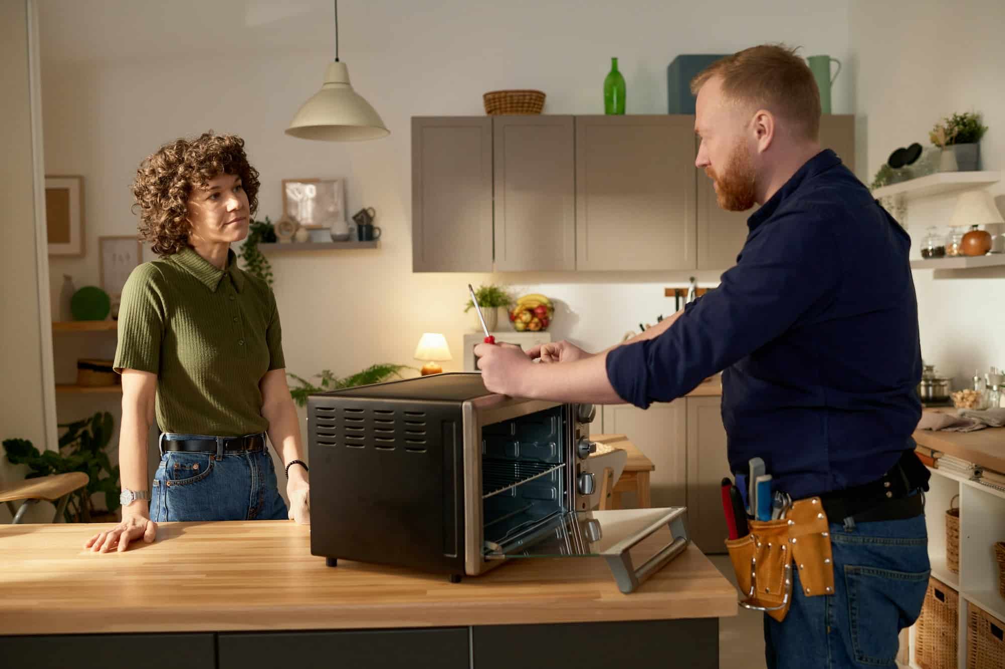 Technician providing appliance repair service in Destin, FL while explaining oven issues to a customer in a modern kitchen.