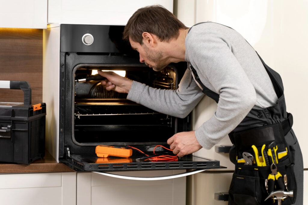 a repairman is repairing a Oven in a kitchen with his tools.