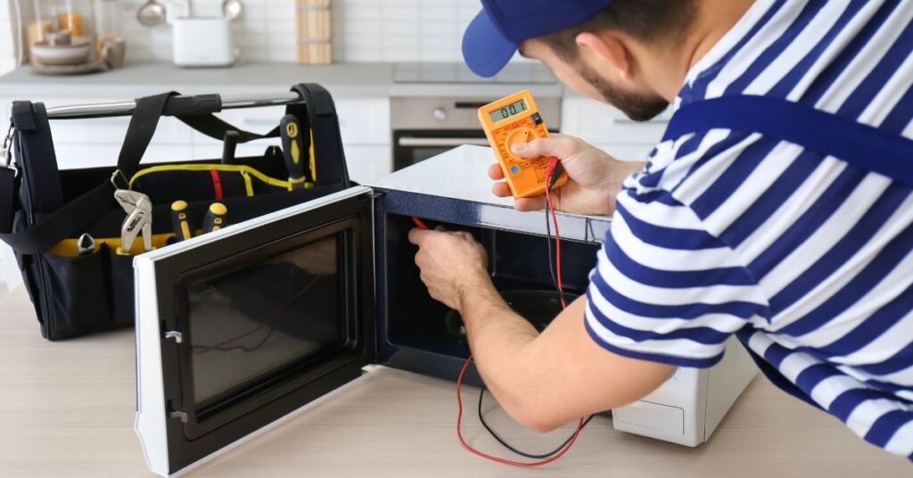 A technician diagnosing a microwave with tools in a kitchen.
