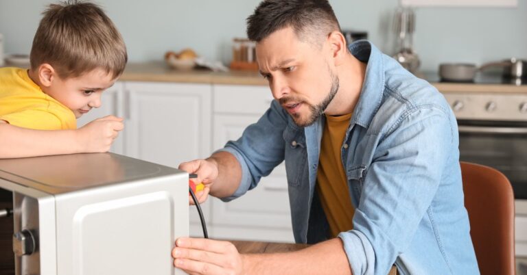A man and a child repairing a noisy microwave in a kitchen.