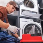 A technician wearing gloves and a uniform provides dryer repair service, working on a dryer unit in a laundry room.