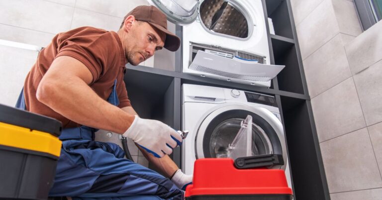 A technician wearing gloves and a uniform provides dryer repair service, working on a dryer unit in a laundry room.